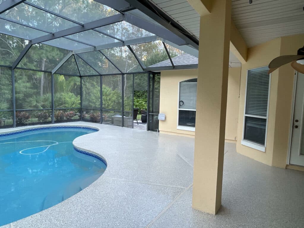 A screened patio enclosure with a kidney-shaped swimming pool. The house has beige walls, white trim, and a speaker mounted outside. There's lush greenery outside.